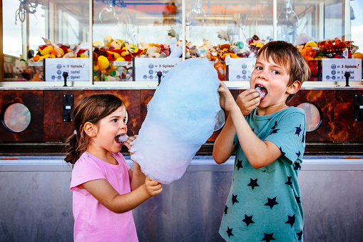 Photo of a brother and sister eating a big cotton candy at an amusement park.