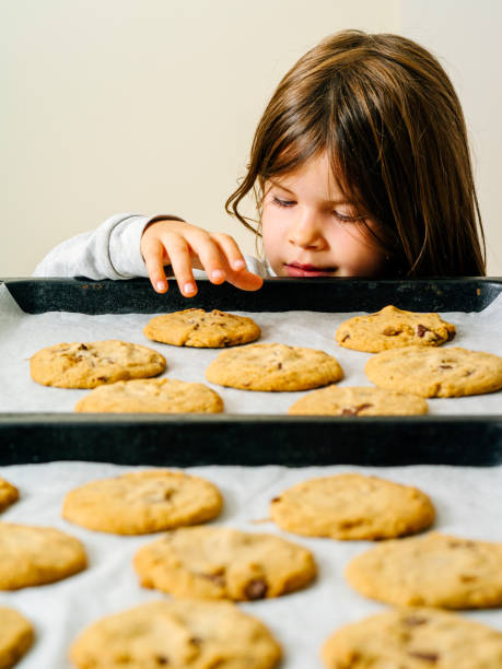 istock Young girl grabbing cookies from a baking tray 1165334097