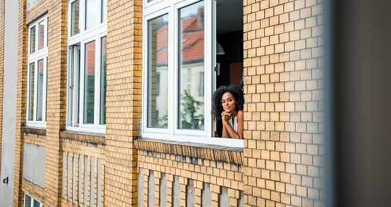 Happy African business woman standing at window and admiring the view