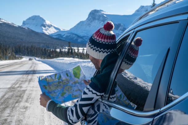 Young man looks at road map from insider car on snowy mountain road- road trip Young man in car on mountain road looks at map for directions. Mountain landscape in winter with snow covering road and pine trees. road map of canada stock pictures, royalty-free photos & images