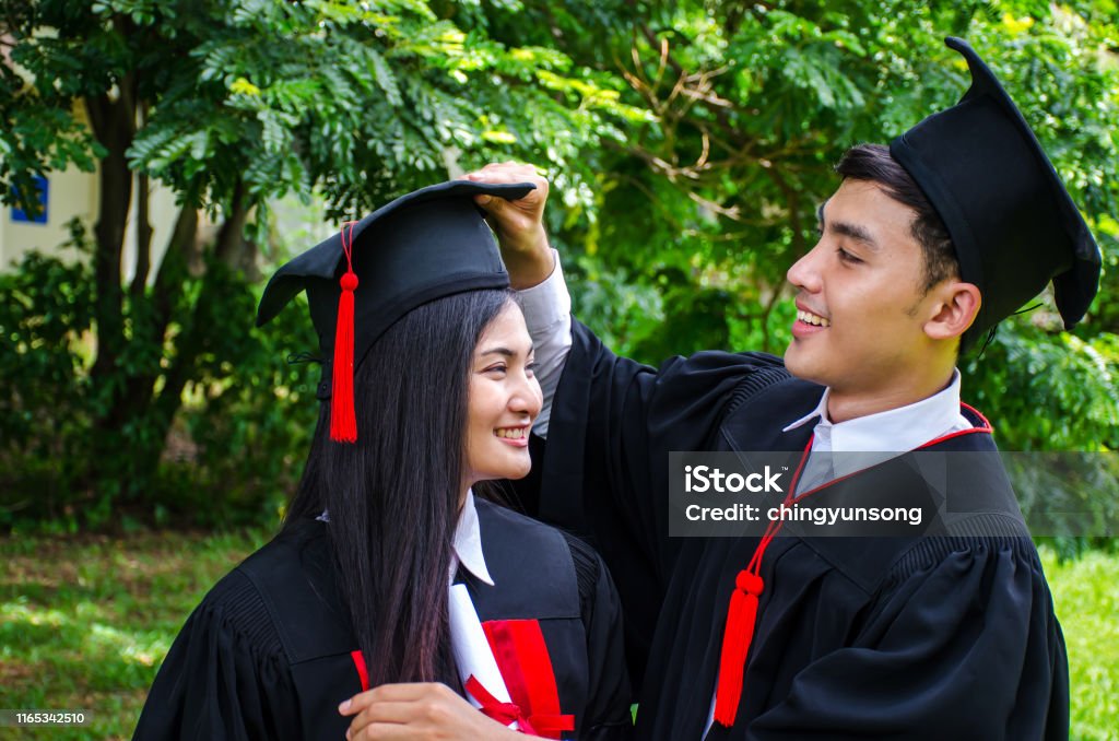 Una Pareja De Hombres Y Mujeres Vestidas Con Vestido Negro De Graduación O  Graduados Con Felicitaciones Con Sombreros De Graduación Está De Pie  Sonriendo Y Sosteniendo Sombrero Con El Fondo Del Parque