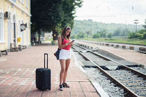 Young girl waiting for train transport on train station outdoor and using smart phone.