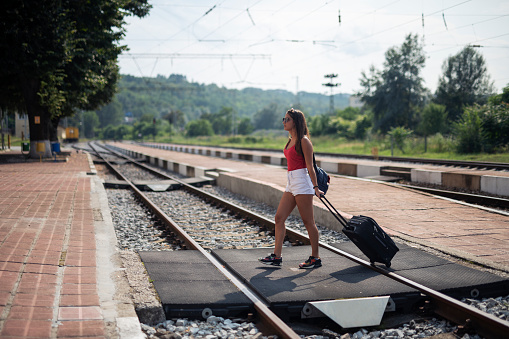 Young woman walking on train station outdoor with suitcase.