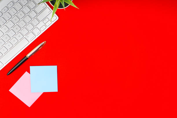 istock Flat lay, top view office table desk. Workspace with pen, decoration vase, sticky notes and keyboard on the red background 1165344794