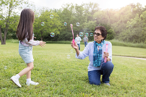 Active senior woman and her granddaughter plays with bubbles with her adorable granddaughter in a park.