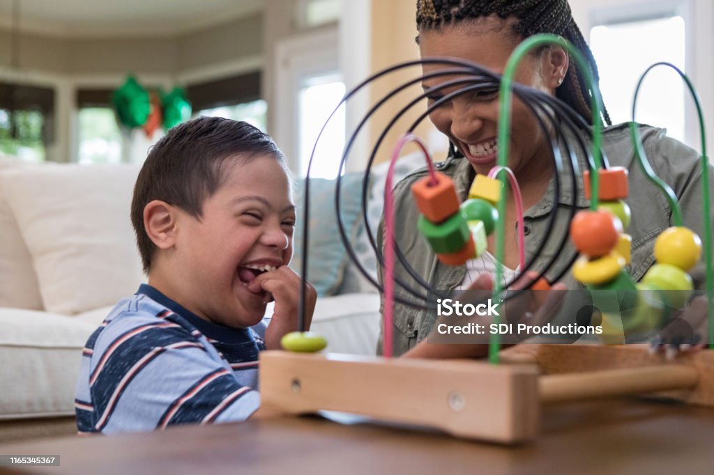 Mom and son laugh together while playing in living room When the mid adult mom and her special needs son play in the living room, they laugh together. Child Stock Photo