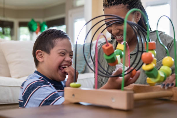 Mom and son laugh together while playing in living room When the mid adult mom and her special needs son play in the living room, they laugh together. down syndrome photos stock pictures, royalty-free photos & images