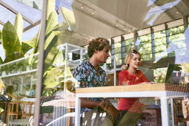 Lifestyle shot of two candid young diverse multi-ethnic millennials working and meeting together in a bright tropical restaurant office space stock photo