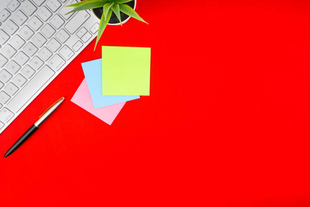 istock Flat lay, top view office table desk. Workspace with pen, decoration vase, sticky notes and keyboard on the red background 1165346470