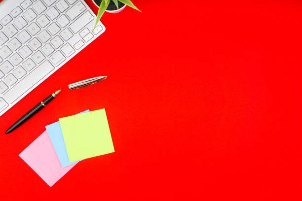 istock Flat lay, top view office table desk. Workspace with pen, decoration vase, sticky notes and keyboard on the red background 1165346527