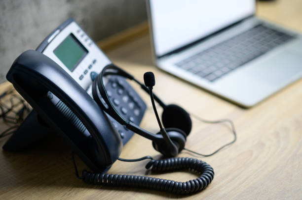 istock IP telephone with headset and laptop computer on wood table, office work space 1165347485