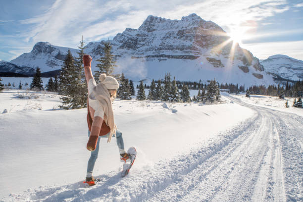 日没時に雪山でスノーシューイングを楽しみ、冬休みを楽しむ女性、腕を伸ばした - rocky mountains canada mountain winter ストックフォトと画像