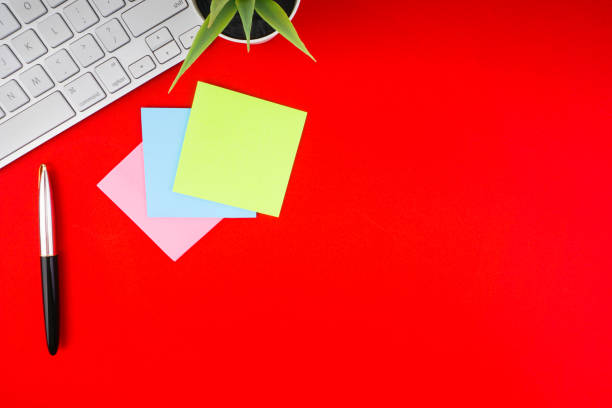 istock Flat lay, top view office table desk. Workspace with pen, decoration vase, sticky notes and keyboard on the red background 1165347600