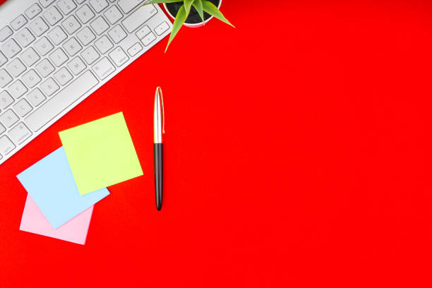 istock Flat lay, top view office table desk. Workspace with pen, decoration vase, sticky notes and keyboard on the red background 1165347637