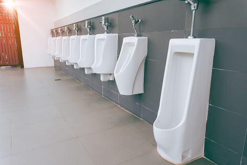 Men's room with white porcelain urinals in line. Modern clean public toilets with tiles . Comfort male toilet urinal concept.