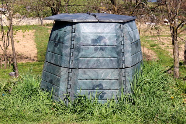 istock Plastic compost bin with dilapidated faded color surrounded with uncut grass and trees in local urban garden 1165356138