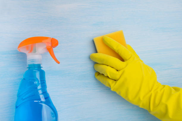 istock on a blue background, a hand in a yellow glove cleans the surface with a sponge, next to a bottle with a spray of cleaning liquid 1165356765