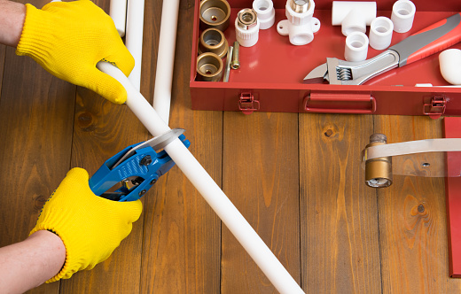 on a dark wooden background and tools, the hands of a worker in yellow gloves, scissor a white plumbing pipe