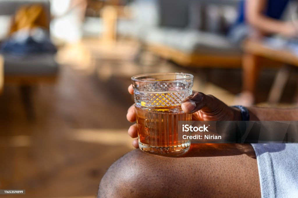 Hand holding glass with Old Fashioned cocktail African ethnicity man's hand holding glass with Old Fashioned cocktail. Rum Stock Photo