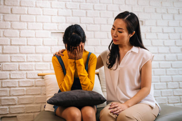 Asian mother comforting crying teenage daughter in miserable, stressed, depressed, sad state of mind Asian mother comforting crying teenage daughter in miserable, stressed, depressed, sad state of mind. 40s Mom is putting hands over this adolescent teenager shoulders at indoors room. disappointment photos stock pictures, royalty-free photos & images