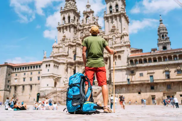 Photo of Young backpacker man pilgrim standing on the Obradeiro square (plaza) - the main square in Santiago de Compostela as a end of his Camino de Santiago pilgrimage.