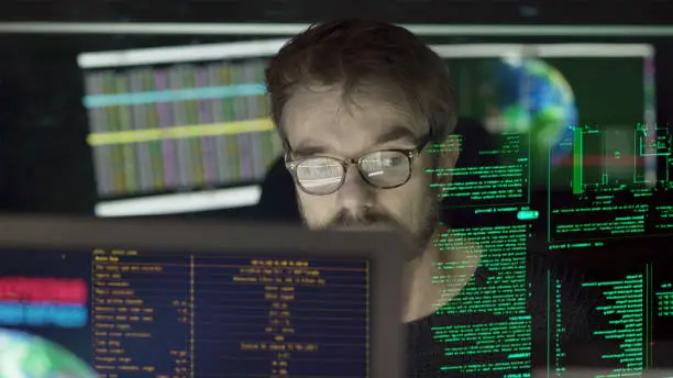 Stock close-up photo of a mature man surrounded by monitors & a holographic display which he is reading.