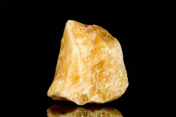 Raw orange calcite mineral stone in front of black background, mineralogy and esotericism