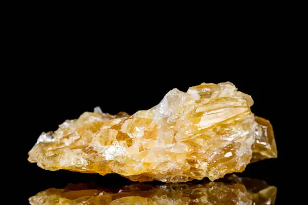 Raw honey calcite mineral stone in front of black background, mineralogy and esotericism