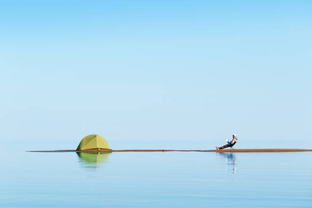 Island. A man sitting on a chair and reading a book. Near the tent.