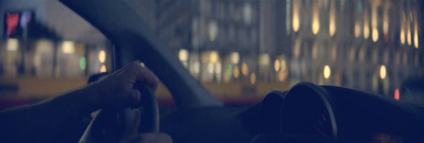 istock Man driving through city at sunset. Hands on wheel 1165368309