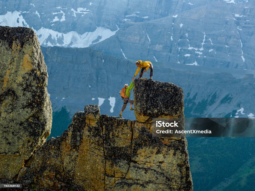 Mountaineers scale rocks steps on cliff with rope Snowcapped mountain behind them Mountain Stock Photo