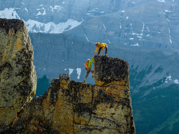 Mountaineers scale rocks steps on cliff with rope Snowcapped mountain behind them canadian rockies photos stock pictures, royalty-free photos & images