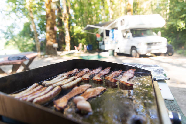 Hot breakfast cooking on outdoor flat grill while camping Hot breakfast on a flat grill outside featuring bacon and sausage griddle stock pictures, royalty-free photos & images