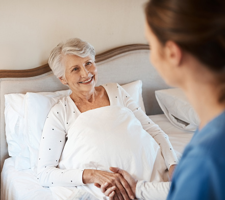 Shot of a young nurse chatting with a senior woman in bed at a retirement home