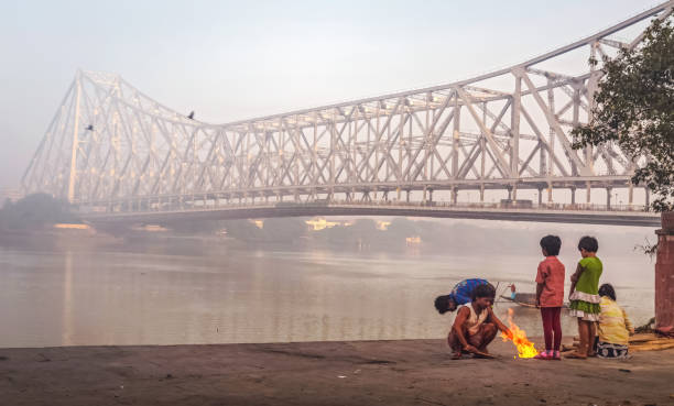 Street dwellers keeping warm by burning fire on a winter morning near the Historic Howrah bridge at Kolkata, India Kolkata, India, December 11,2016: Street dwellers keep warm burning fire on a cold foggy winter morning at Mallick ghat near Howrah bridge at the bank of river Ganges ghat photos stock pictures, royalty-free photos & images