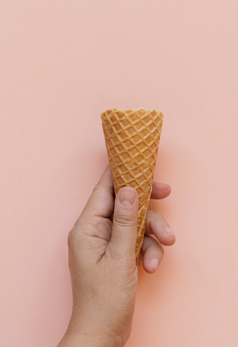 Woman hand holding a empty ice cream cone on pink background