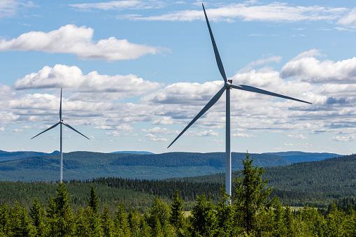 Two windmills in a forest in Northern Sweden with a blue sky with some clouds in background.