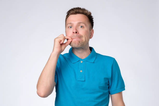 istock Young man closing mouth and lips shut as zip with fingers. 1165392998