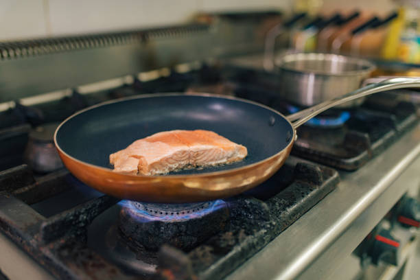Skilled male chef, in the kitchen, transferring the grilled sea bass from the cooking pan into the plate