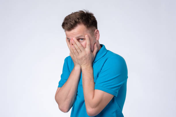 istock Man in blue t-shirt hiding cover face with hands, looking shy 1165400169