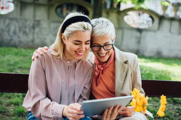 мать и дочь с помощью цифрового планшета - senior women senior adult bench flower стоковые фото и изображения