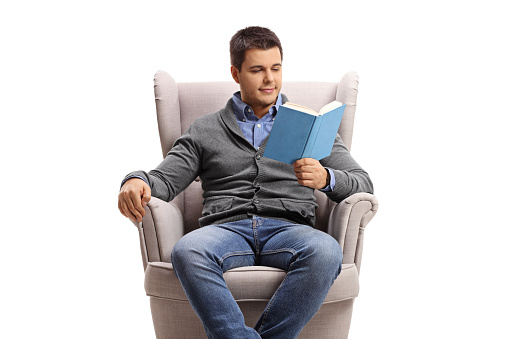 Young man in an armchair reading a book isolated on white background