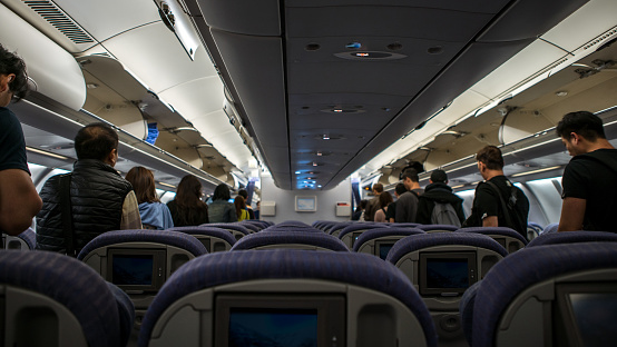 Interior airplane, passengers in aisle are walking to get off airplane. People travelling with the suitcase for business or tourism. Male and female passengers
