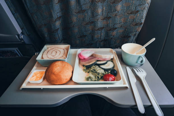 기내식 이코노미 클래스. 항공사. 기내 에서 먹을 수 있습니다. 승객에게 먹이를 줄 수 있습니다. 음식 세트 클로즈업 상단 보기. 비행기의 접이식 테이블에 접시에 샐러드와 빵과 디저트소시지 - filter feeder 뉴스 사진 이미지