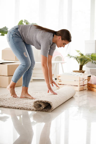 istock Happy young woman rolling a carpet while packing for a move 1165422482