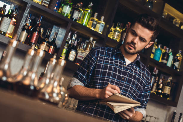 Young bartender standing at bar counter planning shopping list