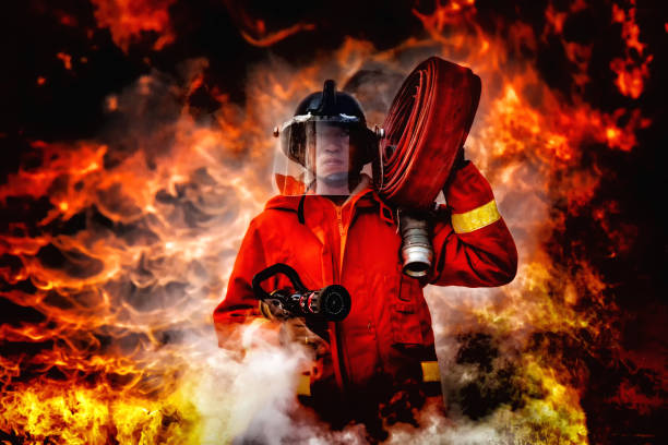 istock fireman wearing firefighter suit holding a fire hose and nozzle to using water and extinguisher to fighting with fire flame in an emergency situation., burning building in background. 1165428582