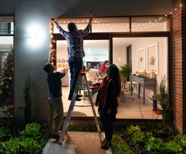 familie versieren het huis voor kerstmis en hangende lichten - hangen stockfoto's en -beelden