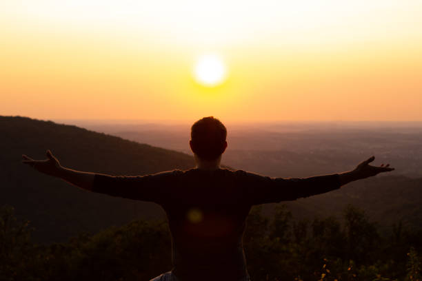 istock Man with open arms embracing sunset over mountain landscape 1165438571