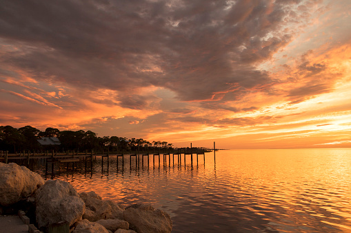 The sun sets over Apalachicola Bay, Florida, overlooking the rocks and a pier on St George Island.